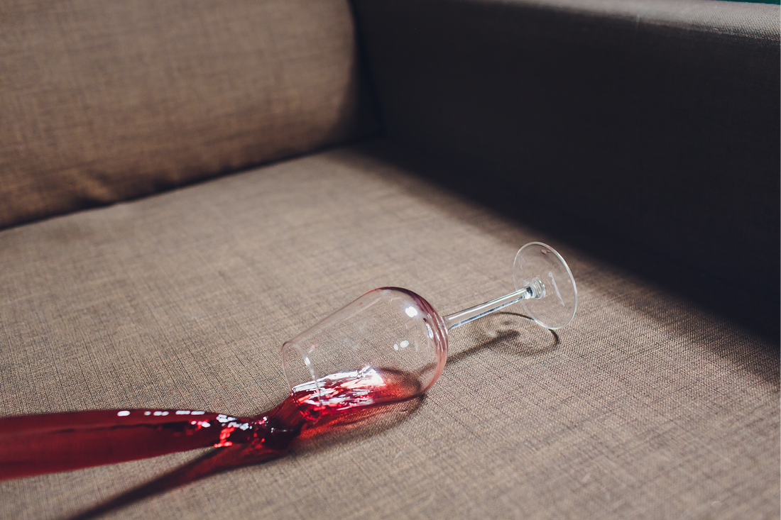 Bicchiere rovesciato con macchia di vino rosso su divano in tessuto